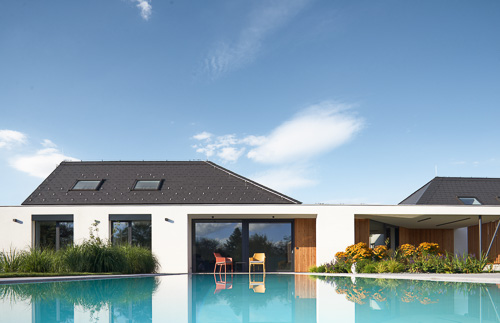 Architektura rodinného domu od AIR Atliér s luxusním bazénem a střechou kopírující okolí.