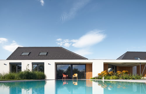 Architektura rodinného domu od AIR Atliér s luxusním bazénem a střechou kopírující okolí.